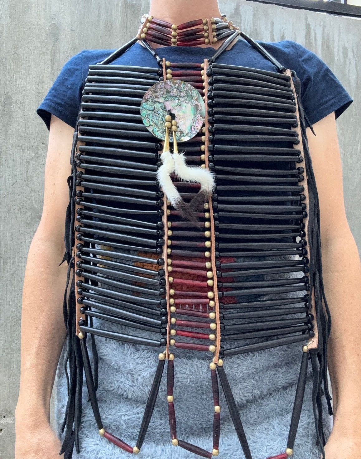 Person wearing an Indian-style beaded breastplate with leather fringe against a gray background