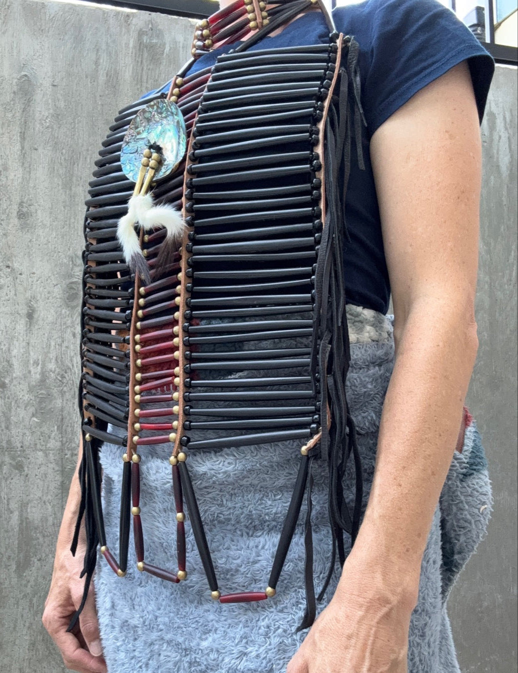 Person wearing an Indian-style beaded breastplate with leather fringe against a gray background